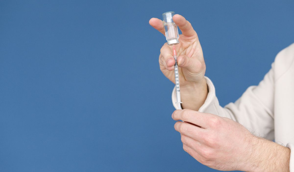 Healthcare worker drawing liquid from a vial into a syringe.