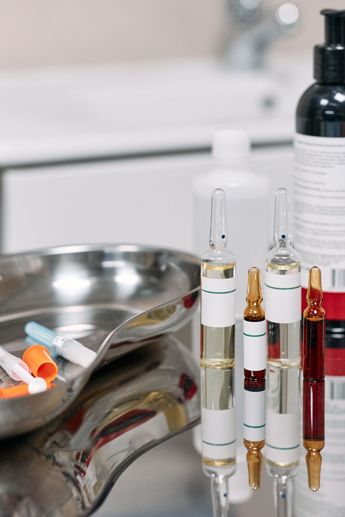 Medical ampoules and syringes beside a metal tray.