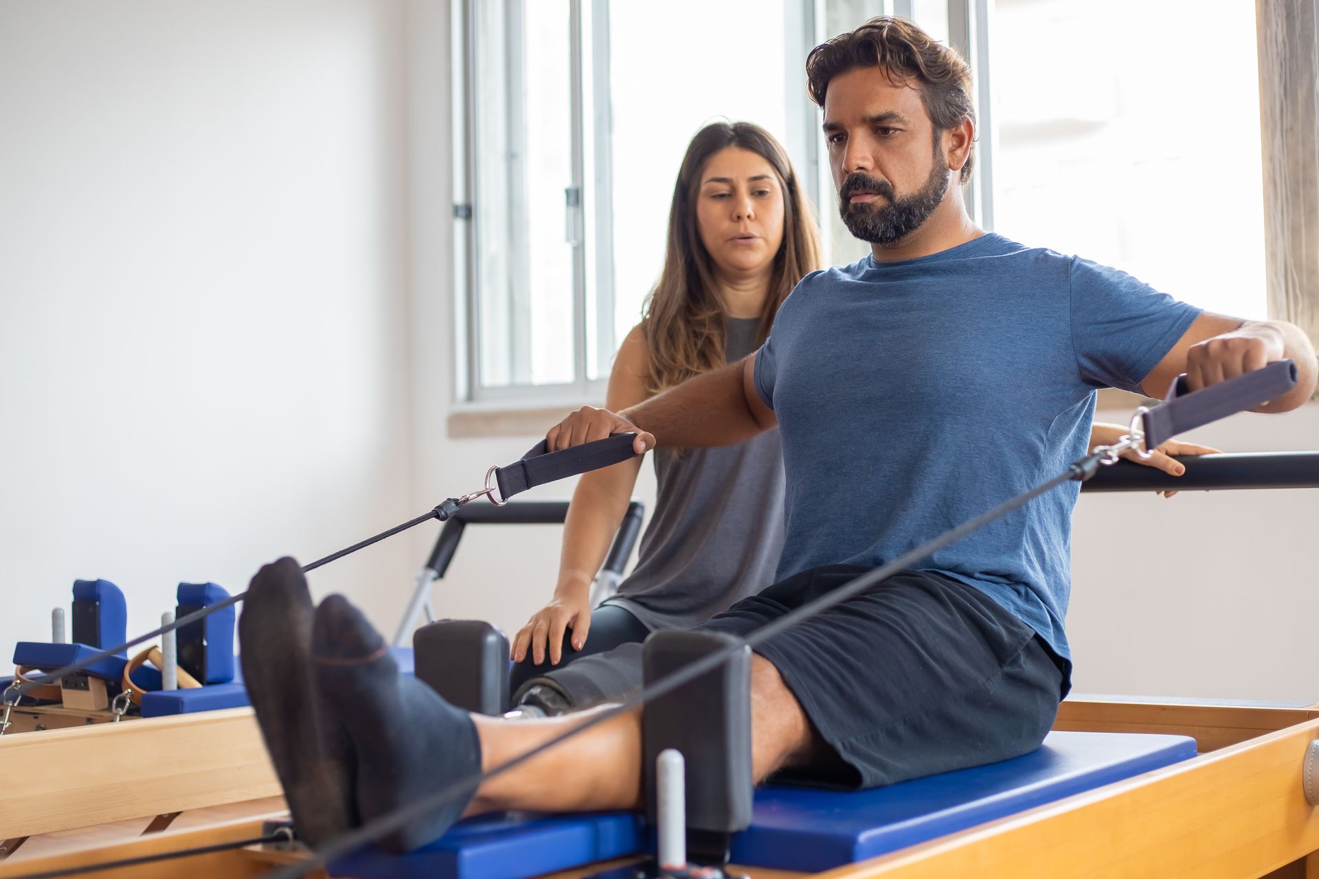 Man exercising on a Pilates reformer with an instructor.