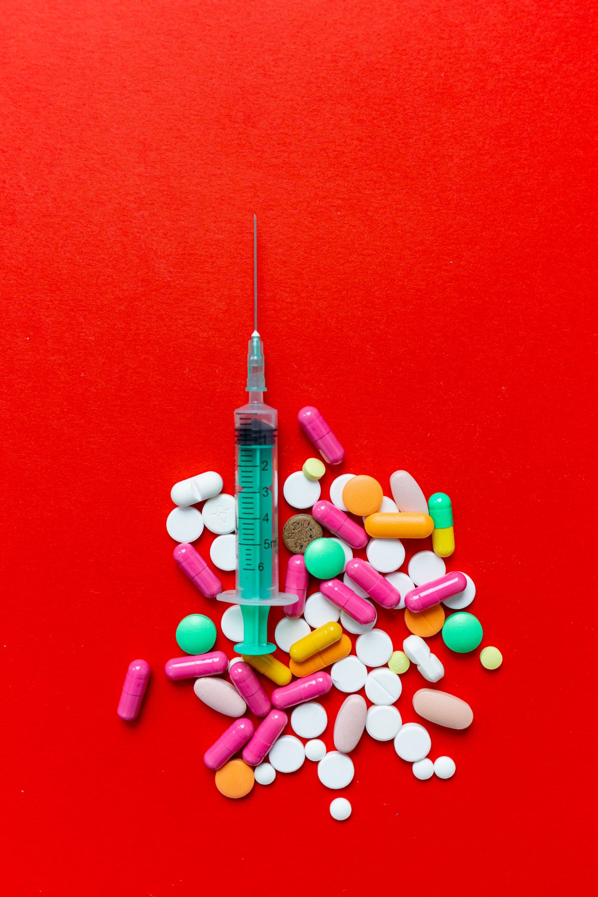 Tablets and a syringe arranged on a red background.